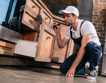 pest control worker examining kitchen with flashlight